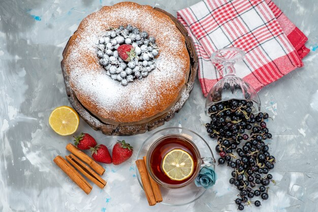 A top view fruit cake delicious and round formed with fresh blue, berries and tea on bright cake biscuit sweet sugar