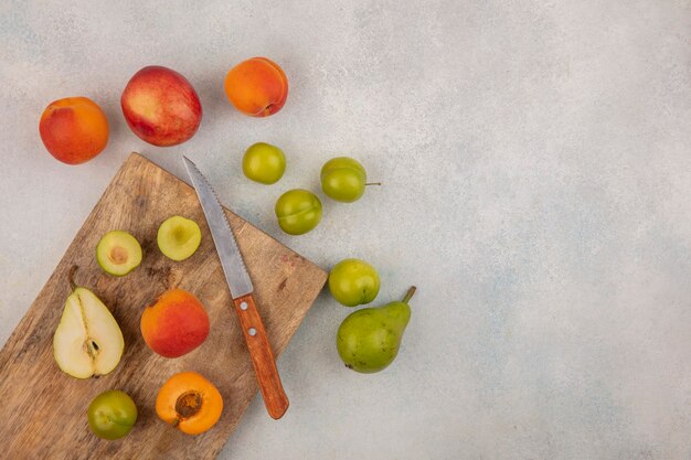 Top view of fruits as half cut pear plum apricot with knife on cutting board and pattern of pear plum apricot peach on white background with copy space