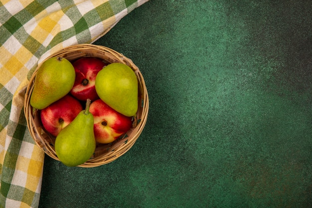 Free photo top view of fruits as peach and pear in basket with plaid cloth on green background with copy space