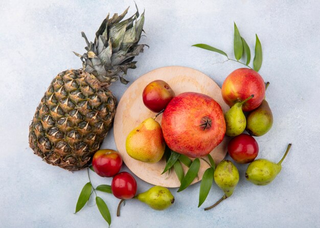 Top view of fruits as plum peach and pomegranate on cutting board and with apple and pineapple on white surface