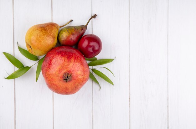 Top view of fruits as plum pomegranate peach with leaves on wooden surface with copy space