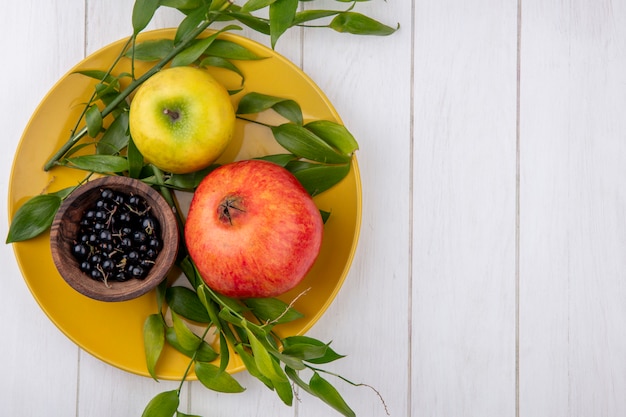 Free photo top view of fruits as pomegranate apple and bowl of blackthorn berries with leaves in plate on wooden surface with copy space