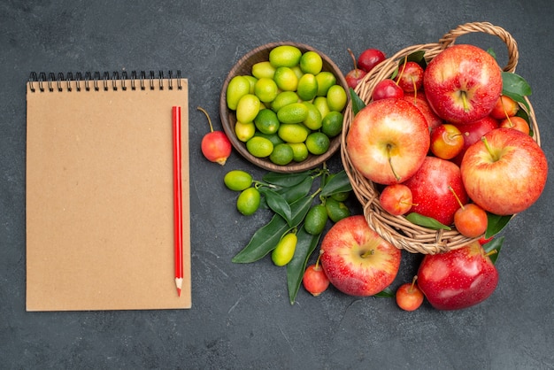 Top view fruits citrus fruits wooden basket of cherries apples cream notebook red pencil