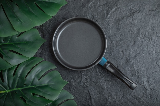 Free Photo top view of frying pan over black background with green leaves.