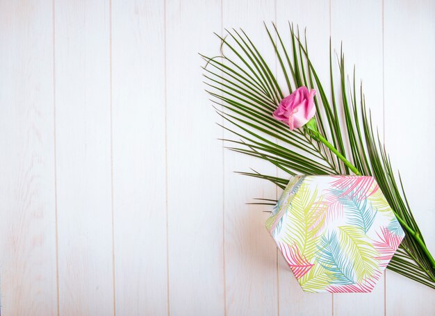 Top view of a gift box with pink color rose and palm leaf on white background with copy space