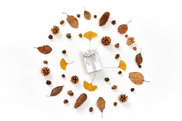 Top view of a gift in the middle of a wreath made of autumn leaves and conifer cones on white