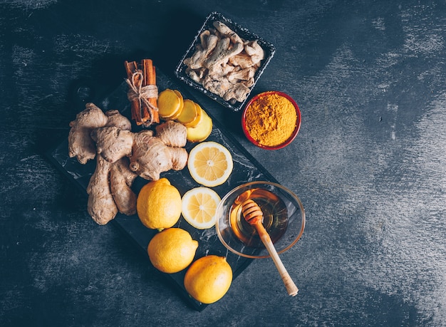 Top view ginger powder with ginger, lemon, honey and dry cinnamon pack on dark textured background. horizontal