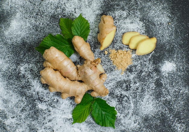 Top view ginger with slices and leaves on gray textured surface. horizontal