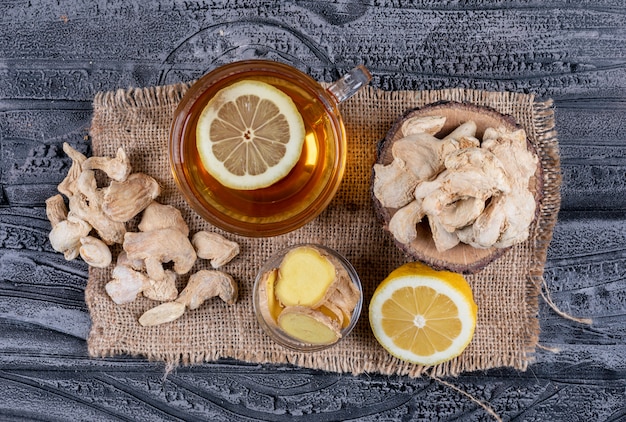 Top view ginger with tea, lemon and ginger slices on sack cloth and dark wooden background. horizontal