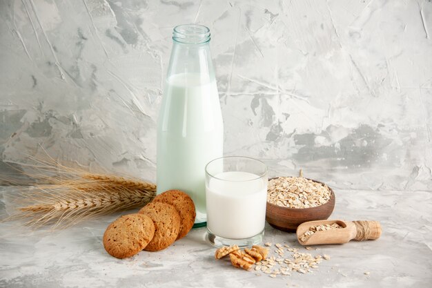 Top view of glass bottle and cup filled with milk on wooden tray and cookies spoon oats in brown pot on white table on ice background