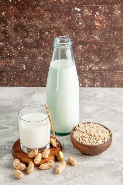 Top view of glass bottle and cup filled with milk on wooden tray and dry fruits spoon oats in brown pot on white table on brown background