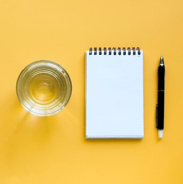 Free photo top view of glass of water with notebook and pen