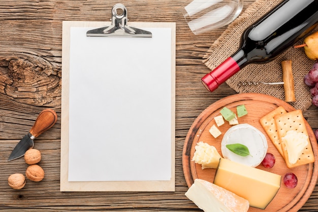 Top view gourmet cheese assortment with wine glass and blank notepad