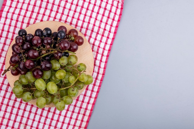 Top view of grapes on cutting board on plaid cloth and gray background with copy space