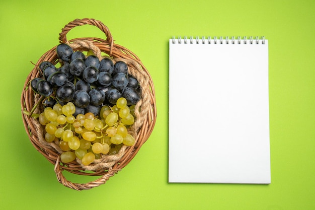 Free photo top view grapes white notebook bunches of grapes on the green table