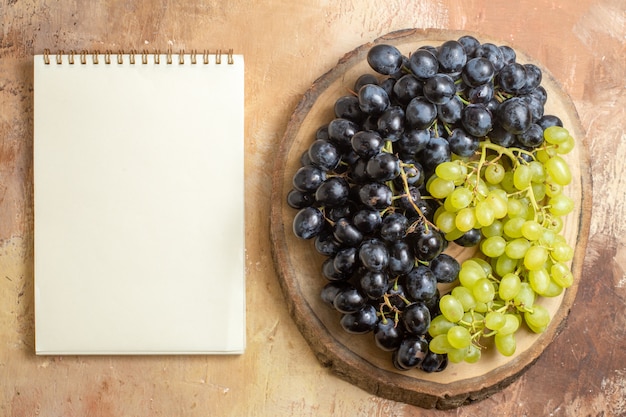 Top view grapes wooden board with green and black grapes next to the white notebook