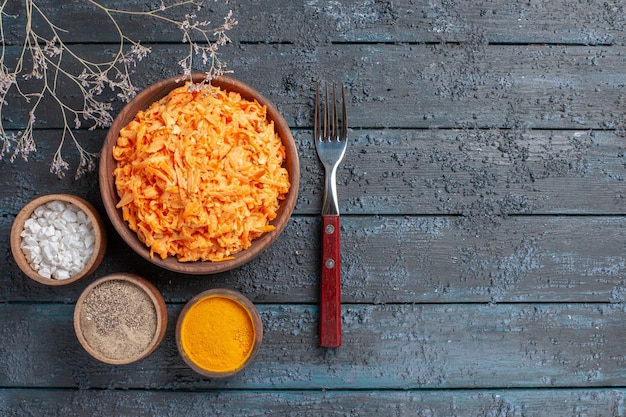 Top view grated carrot salad with garlic and seasonings on a dark-blue rustic desk health color salad ripe vegetable diet