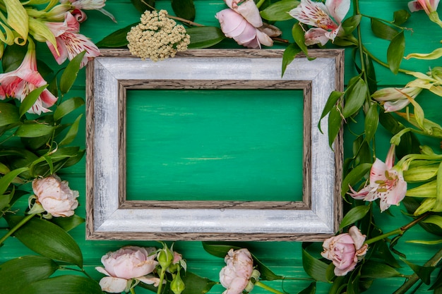 Top view of gray frame with light pink flowers and leaf branches on a green surface