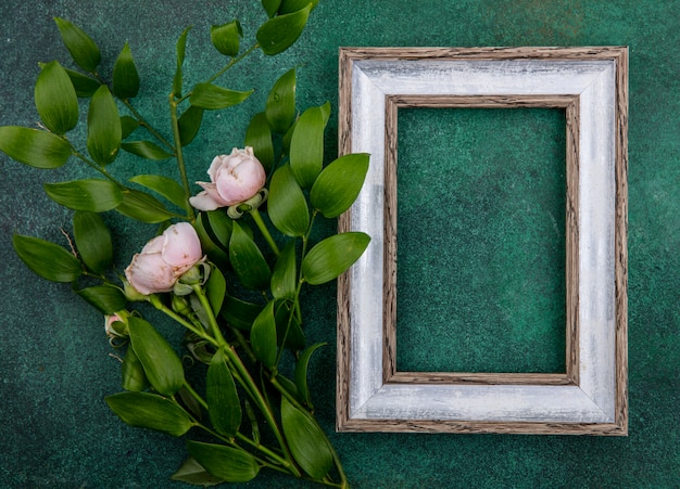 Top view of gray frame with light pink roses and leaf branches on a green surface