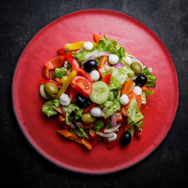 Free photo top view greek salad with tomato and olive and lettuce in red plate