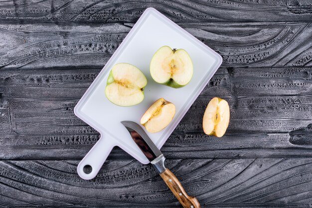 Top view green apples sliced with knife on plastic board on gray wooden table and black