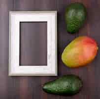 Free photo top view of green avocado with mango on a wooden surface