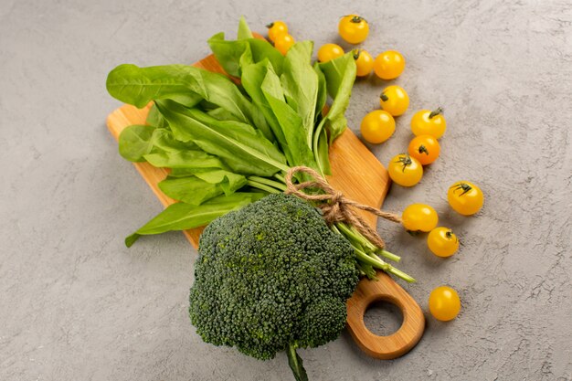 top view green broccoli leafs along with yellow tomatoes on the grey floor