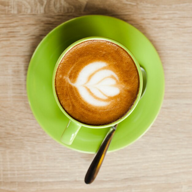 Top view of green coffee cup with beautiful latte art over wooden surface