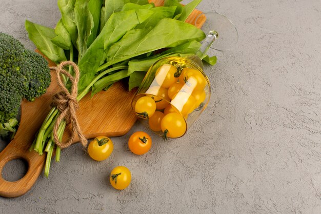 top view green leafs along with broccoli and yellow tomatoes on the grey background