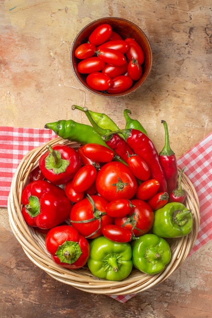 Top view green and red peppers hot peppers tomatoes in wicker basket cherry tomatoes in bowl kitchen towel on amber background