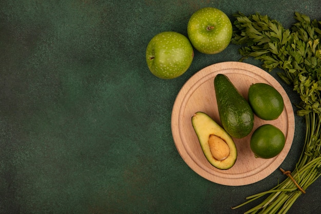 Free Photo top view of green skinned avocados on a wooden kitchen board with limes with green apples and parsley isolated on a green surface with copy space