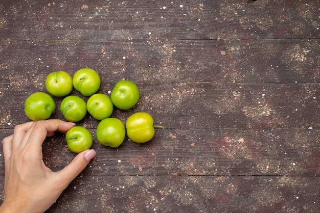 Free photo top view green sour cherry-plums lined mellow and fresh on the wooden rustic background fruit color mellow