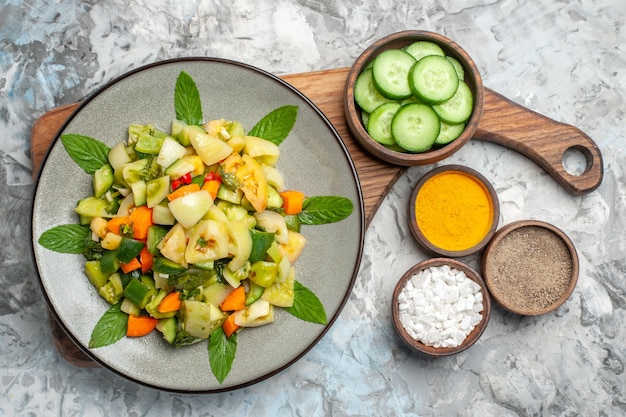 Free Photo top view green tomato salad on oval plate bowl with cut cucumber on cutting board on dark background