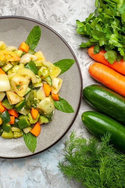 Top view green tomato salad on oval plate different vegetables on dark background