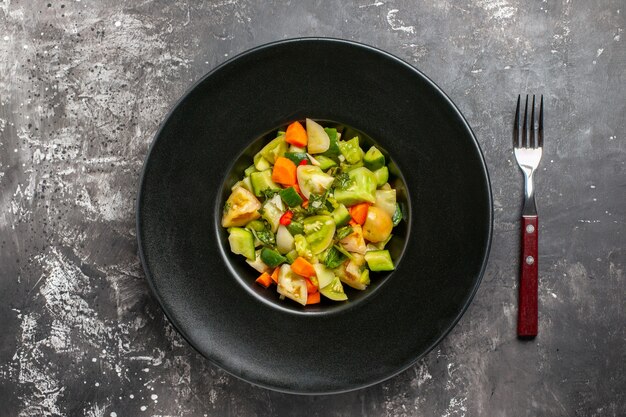 Top view green tomato salad on oval plate a fork on dark background