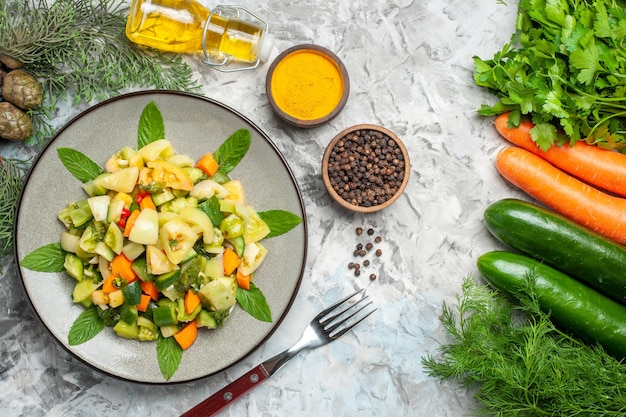 Top view green tomato salad on oval plate a fork spices oil bottle vegetables on dark background