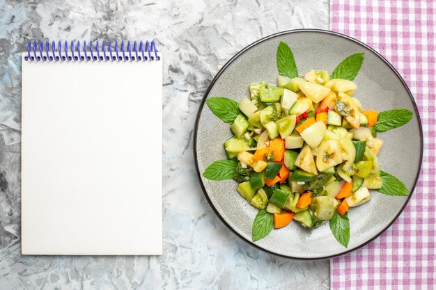 Free Photo top view green tomato salad on oval plate pink tablecloth a notebook on grey surface