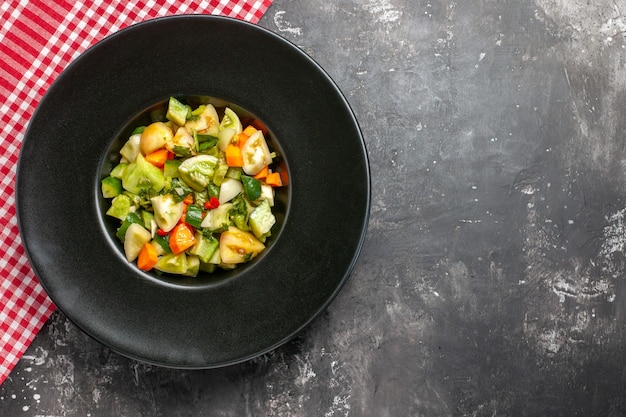 Top view green tomato salad on oval plate red tablecloth on dark surface