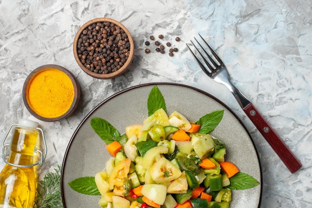 Top view green tomato salad on oval plate with a fork and black pepper oil bottle on dark background