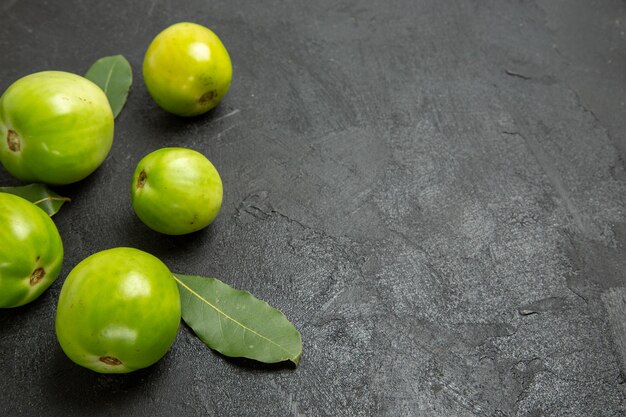 Top view green tomatoes and bay leaves on the left of dark ground with copy space