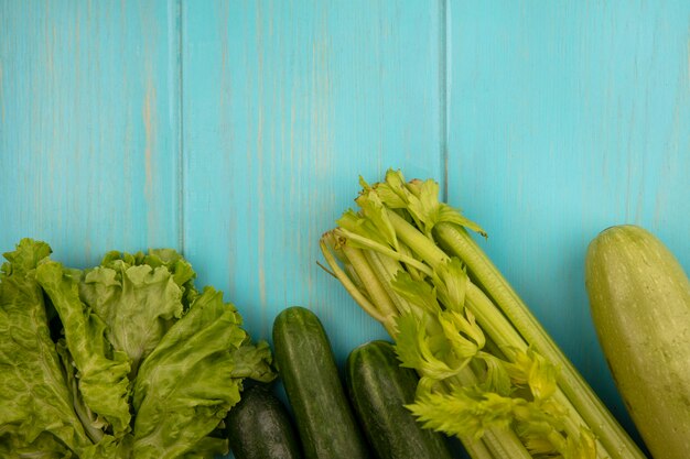 Top view of green vegetables such as cucumbers lettuce zucchinis and celery isolated on a blue wooden wall with copy space