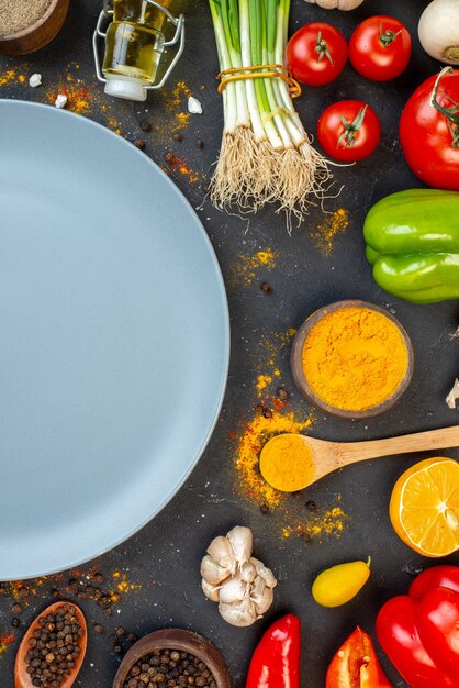 Top view grey round platter vegetables and spices on black table