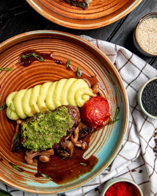 Free photo top view of grilled beef with mashed potatoes tomato mushrooms and avocado sauce in a plate on wood