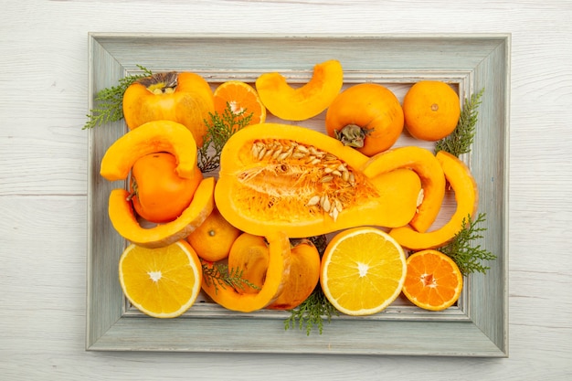 Top view half butternut squash cut orange persimmons mandarins on frame on white table