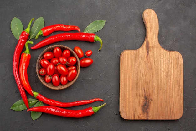 Free photo top view half circle of red hot peppers and bay leaves and a bowl of cherry tomatoes and a chopping board on the black table