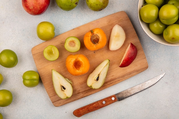 Top view of half cut fruits as plum apricot pear peach on cutting board and whole ones with knife on white background