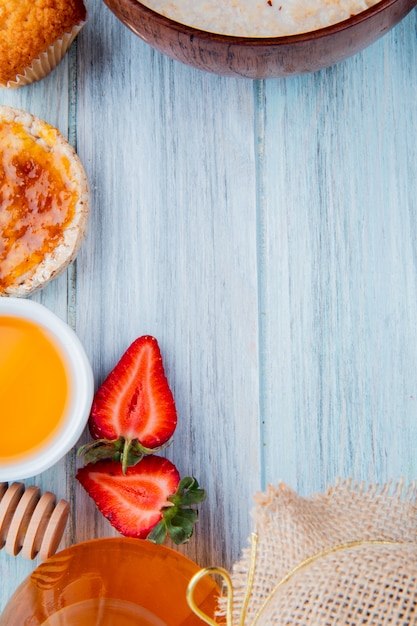 Top view of half cut strawberries with oats crispbread peach syrup cupcake butter on wood with copy space