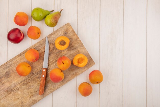 Free photo top view of half cut and whole apricots and knife on cutting board with pattern of fruits as peach apricot and pear on wooden background with copy space