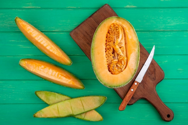 Free Photo top view of halved cantaloupe melon on a wooden kitchen board with knife on green wooden surface