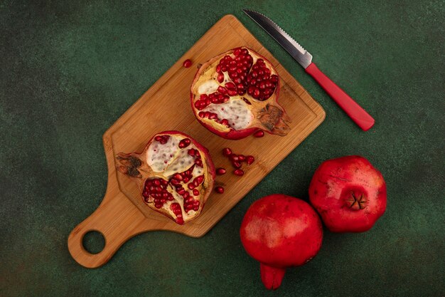 Top view halved pomegranate with knife on cutting board on green wall